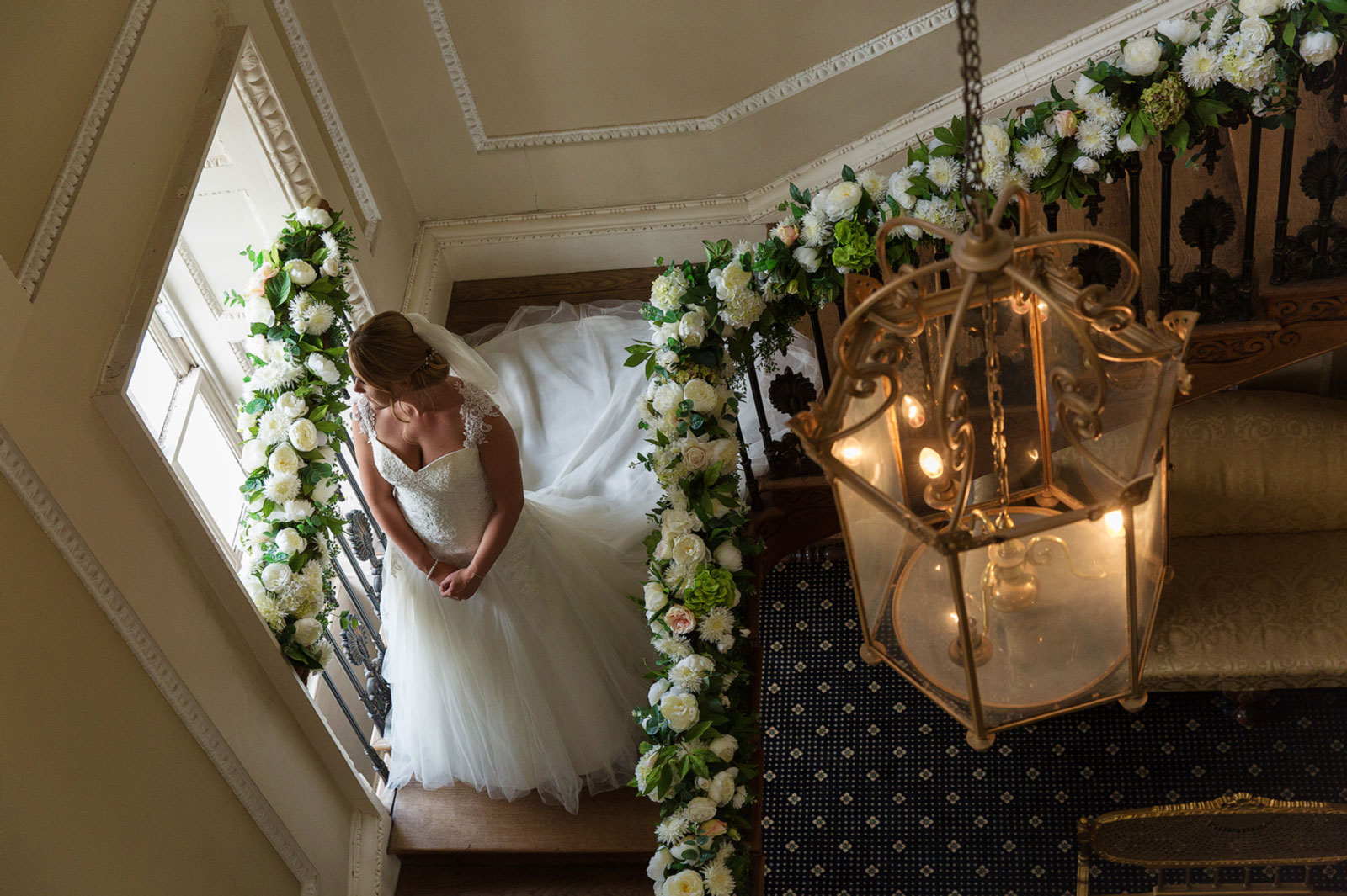 Beautiful bride walking down wooden staircase with flowers in Boreham House