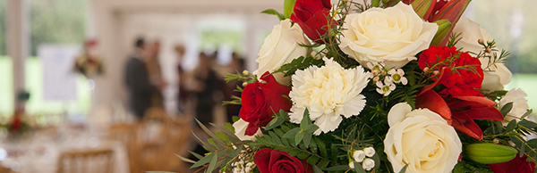 close up view of red and white floral bouquet with bridal party in the background